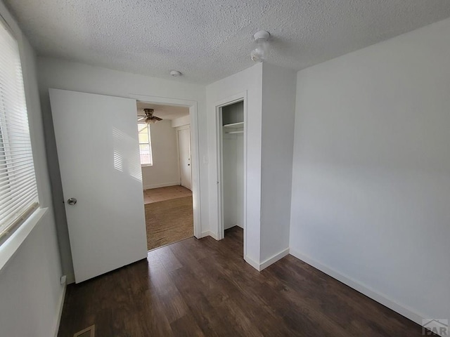 unfurnished bedroom featuring dark wood-style floors, a closet, a textured ceiling, and baseboards