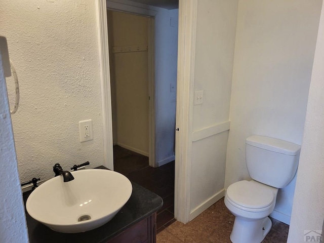 bathroom featuring toilet, a textured wall, baseboards, and vanity