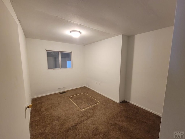 empty room featuring baseboards and dark colored carpet