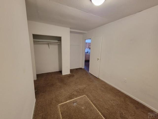 unfurnished bedroom with baseboards, dark carpet, and a closet