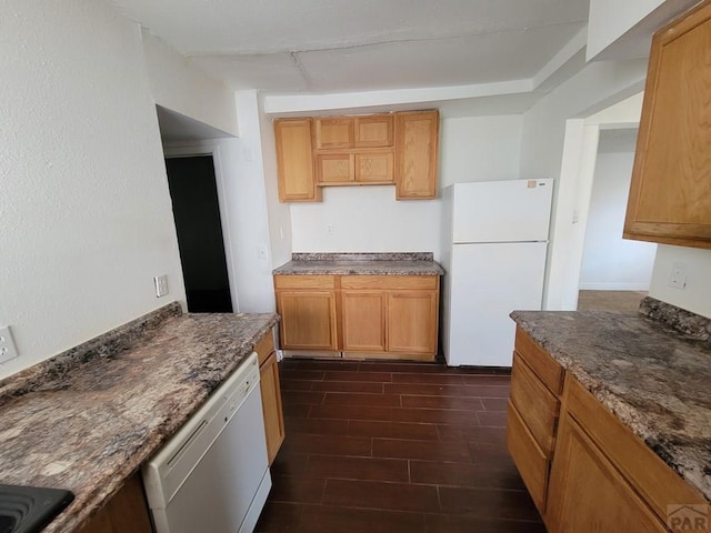 kitchen with dark stone counters, white appliances, and wood finish floors