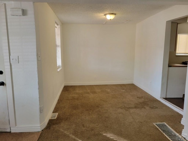 carpeted spare room featuring visible vents, a textured ceiling, and baseboards