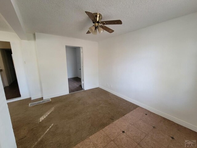 spare room with a textured ceiling, dark carpet, a ceiling fan, and baseboards