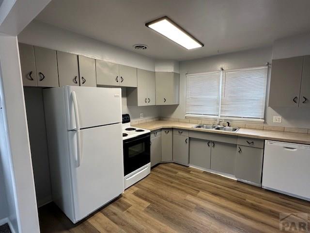 kitchen featuring gray cabinets, wood finished floors, white appliances, light countertops, and a sink
