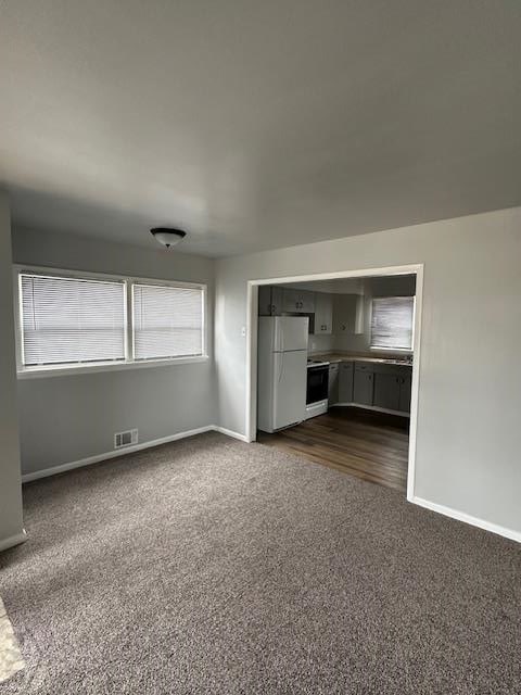 unfurnished living room featuring baseboards, visible vents, and dark carpet