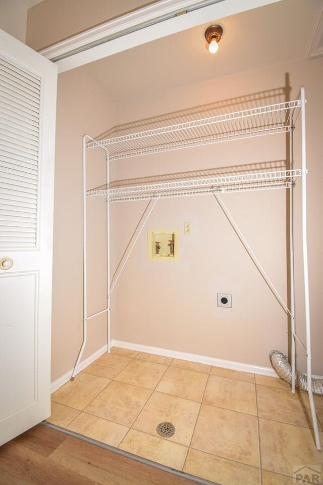 washroom featuring laundry area, electric dryer hookup, washer hookup, baseboards, and light tile patterned flooring