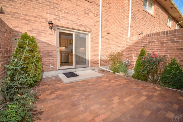 view of exterior entry with fence, a patio, and brick siding