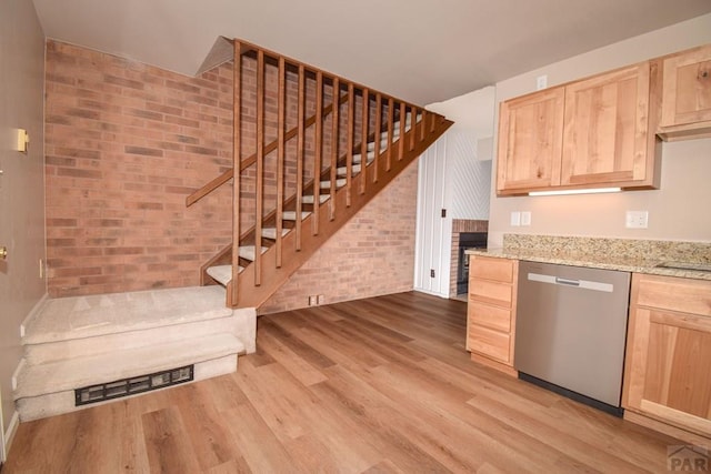 kitchen featuring brick wall, light brown cabinetry, visible vents, light wood-style flooring, and stainless steel dishwasher