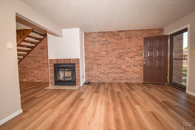 unfurnished living room featuring a textured ceiling, wood finished floors, and brick wall