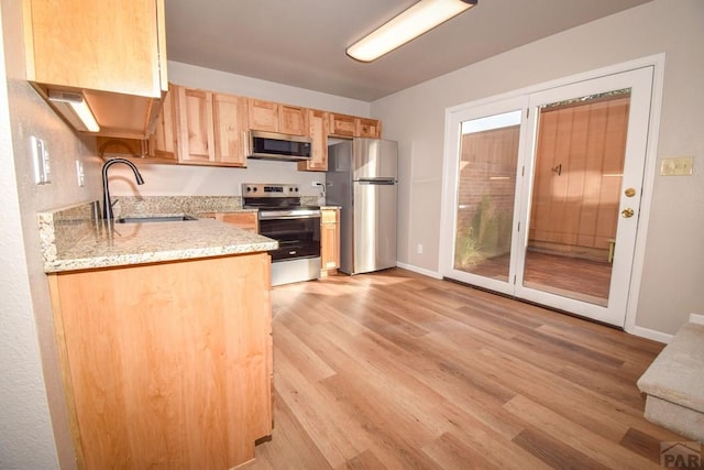 kitchen with a sink, light wood-style floors, light brown cabinets, stainless steel appliances, and baseboards
