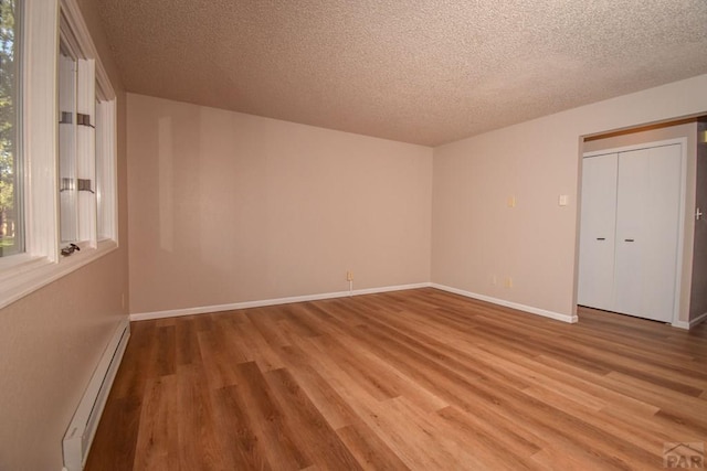 spare room featuring a textured ceiling, baseboard heating, light wood-style flooring, and baseboards