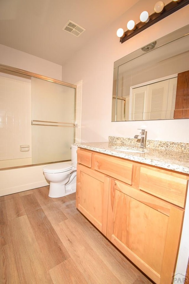 full bath featuring shower / bath combination with glass door, vanity, toilet, visible vents, and wood finished floors