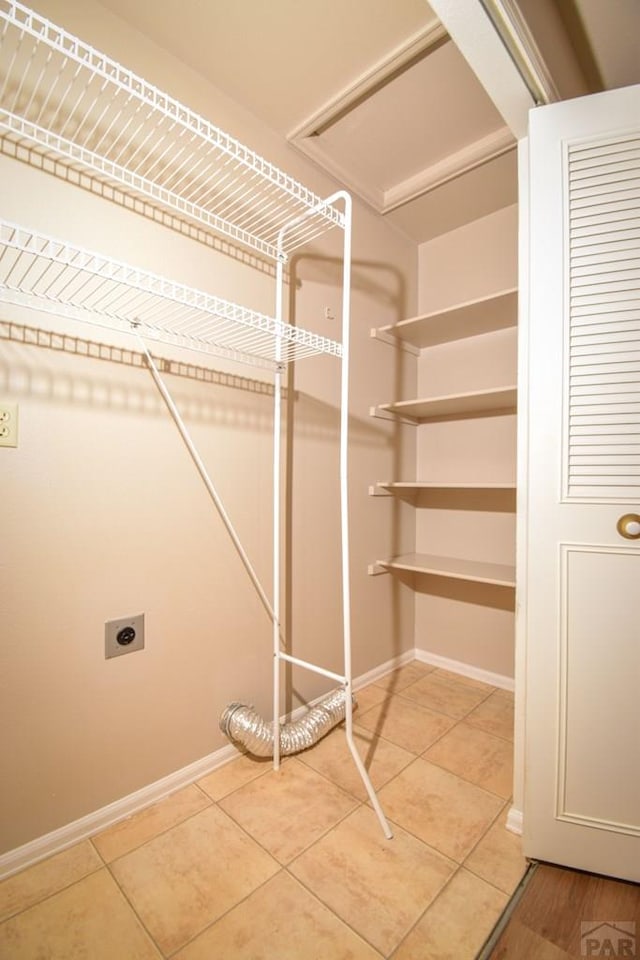 laundry area with hookup for an electric dryer, laundry area, light tile patterned flooring, and baseboards