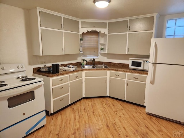 kitchen featuring white appliances, dark countertops, a sink, and light wood-style flooring