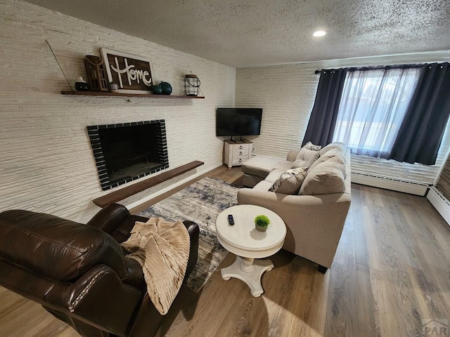 living room with a fireplace, a textured ceiling, baseboard heating, and wood finished floors