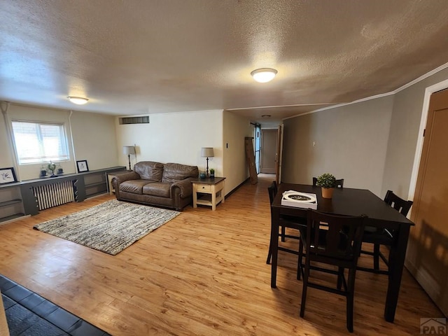 living area featuring radiator heating unit, a textured ceiling, visible vents, and wood finished floors