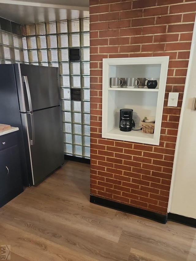 kitchen featuring light wood-style flooring, brick wall, light countertops, freestanding refrigerator, and open shelves