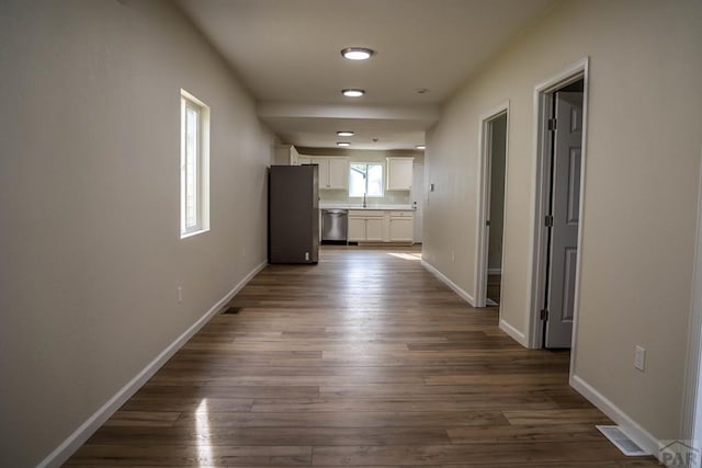 hall with a sink, dark wood finished floors, visible vents, and baseboards