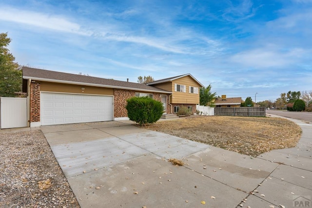 tri-level home with an attached garage, fence, brick siding, and driveway