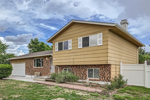 back of property with fence, a yard, an attached garage, brick siding, and a chimney