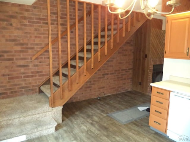stairway with brick wall, an inviting chandelier, and wood finished floors