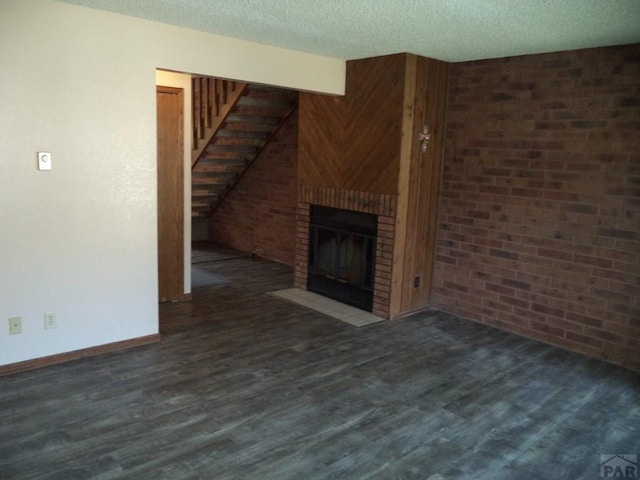 unfurnished living room featuring baseboards, a fireplace, a textured ceiling, wood finished floors, and stairs