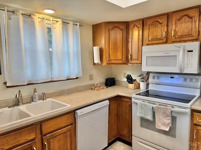 kitchen with brown cabinets, white appliances, light countertops, and a sink