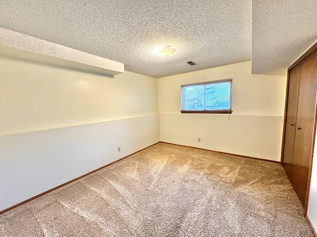 empty room with a textured ceiling, carpet flooring, visible vents, and baseboards