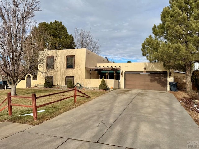 pueblo revival-style home featuring an attached garage, fence, driveway, stucco siding, and a front yard