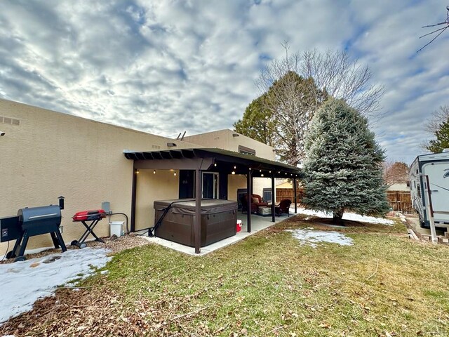 rear view of property with a yard, stucco siding, a hot tub, a patio area, and fence