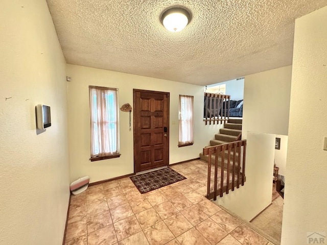 entryway with stairs, baseboards, and a textured ceiling