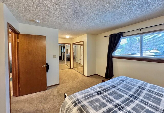 bedroom with light colored carpet, a textured ceiling, and baseboards