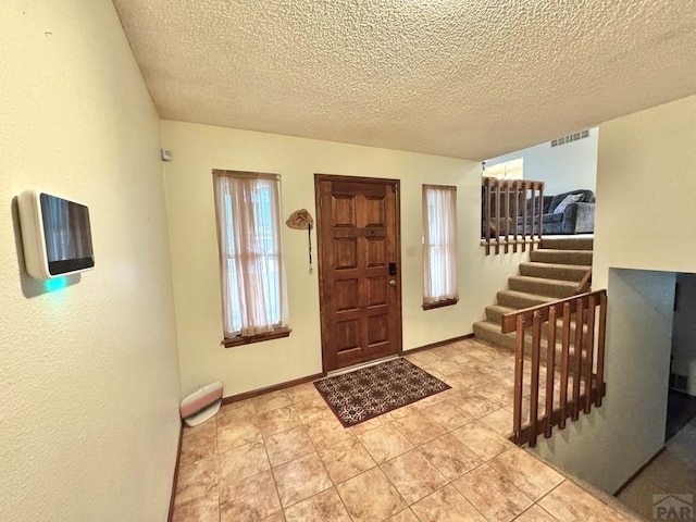 entrance foyer featuring light tile patterned flooring, a textured ceiling, baseboards, and stairs