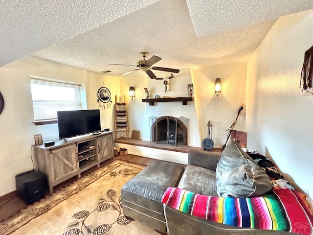 living area with a fireplace with raised hearth, a textured ceiling, and a ceiling fan