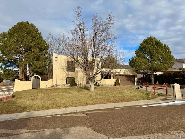 pueblo-style home featuring a front yard, fence, a gate, and stucco siding