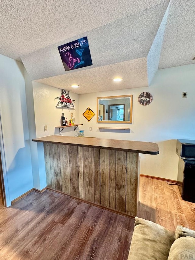 bar featuring wet bar, a textured ceiling, baseboards, and wood finished floors