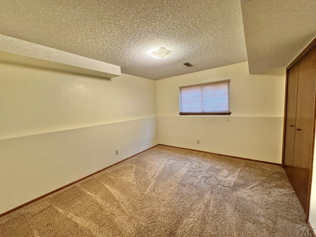 below grade area with a textured ceiling, carpet flooring, visible vents, and baseboards