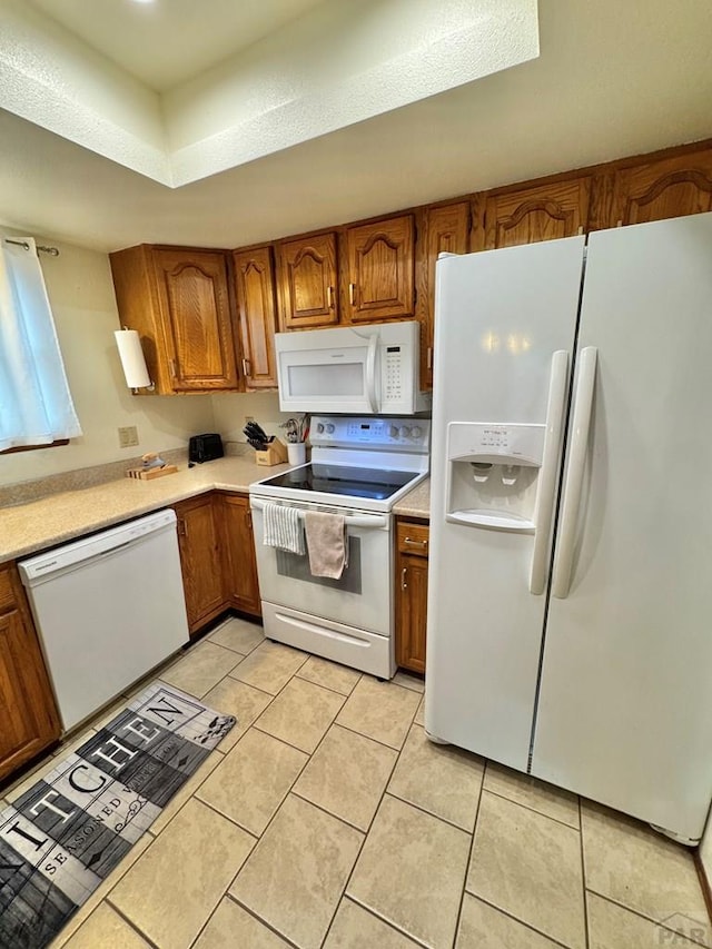 kitchen with light tile patterned floors, light countertops, white appliances, and brown cabinetry