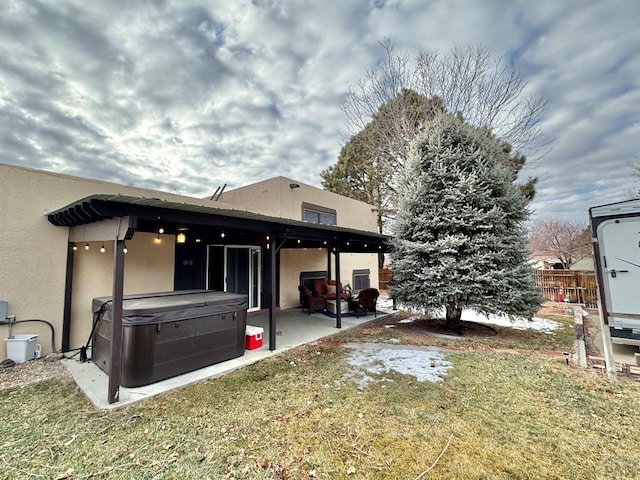 back of property featuring a yard, a patio, stucco siding, a hot tub, and fence