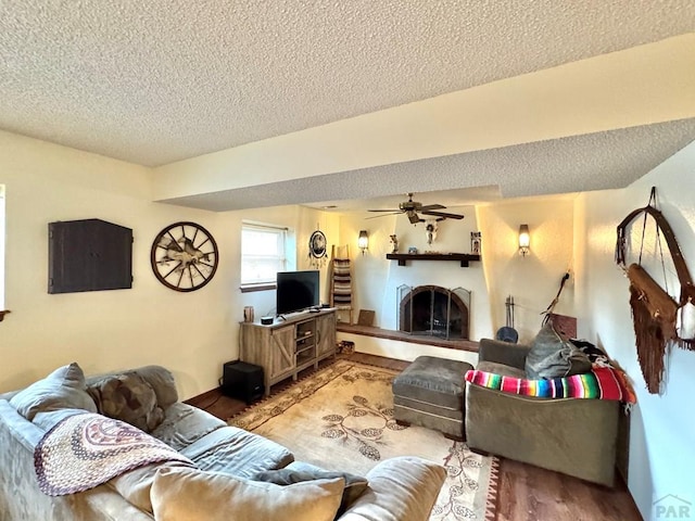 living area with a fireplace with raised hearth, ceiling fan, a textured ceiling, and light wood finished floors