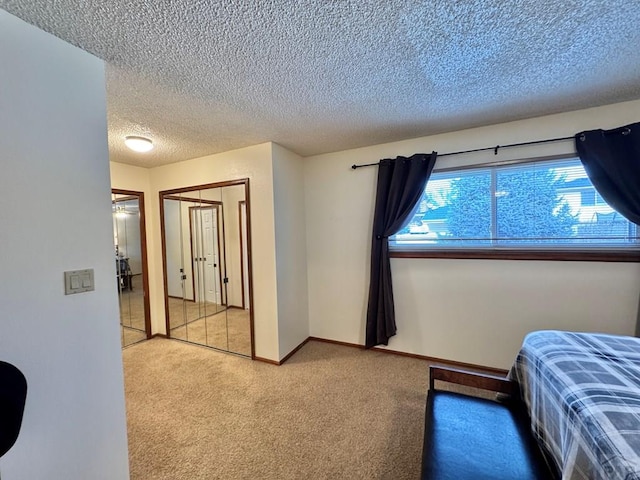 bedroom featuring a closet, light carpet, a textured ceiling, and baseboards