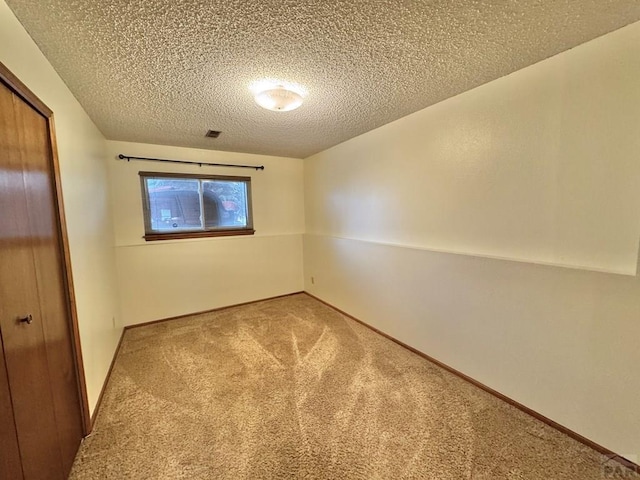 unfurnished room featuring visible vents, carpet flooring, a textured ceiling, and baseboards