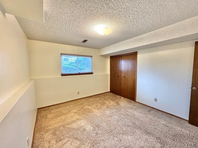 unfurnished bedroom with a closet, light colored carpet, visible vents, a textured ceiling, and baseboards