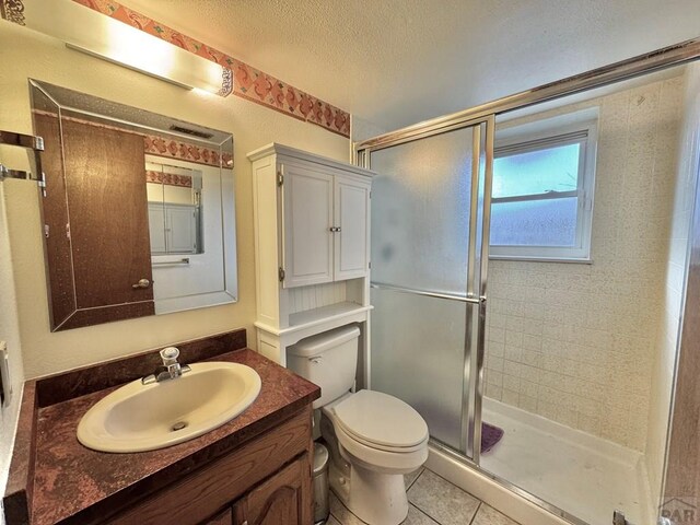 bathroom with toilet, a stall shower, a textured ceiling, vanity, and tile patterned floors