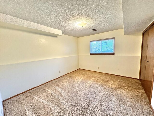 spare room featuring a textured ceiling, carpet, visible vents, and baseboards