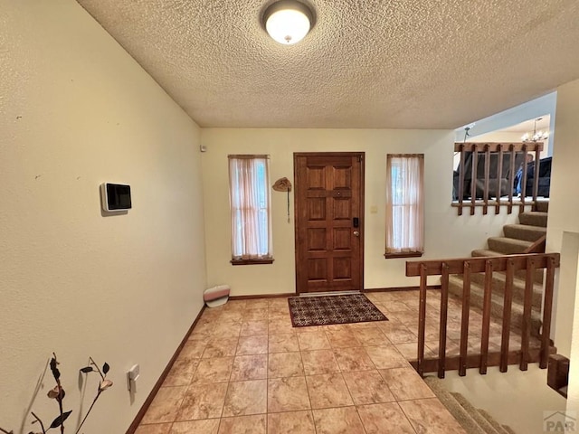 foyer entrance with an inviting chandelier, stairway, baseboards, and a textured ceiling