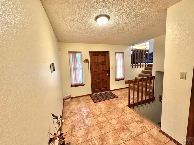 foyer entrance with a textured wall, stairway, and baseboards