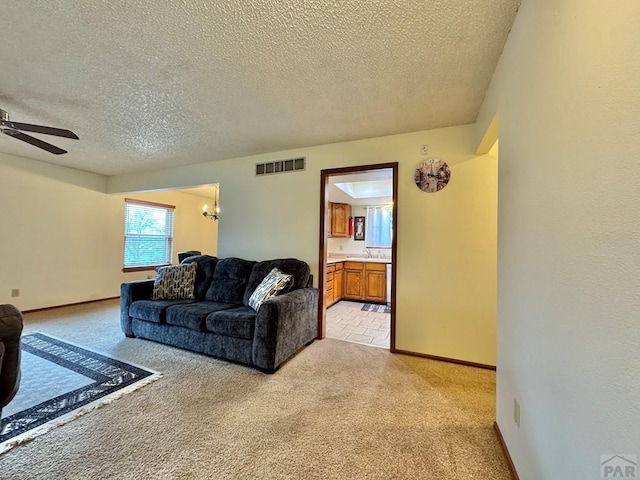 living room with a textured ceiling, light colored carpet, ceiling fan with notable chandelier, visible vents, and baseboards