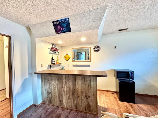 bar with a dry bar, baseboards, visible vents, stainless steel microwave, and wood finished floors