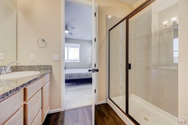 bathroom featuring ceiling fan, wood finished floors, vanity, a stall shower, and ensuite bath